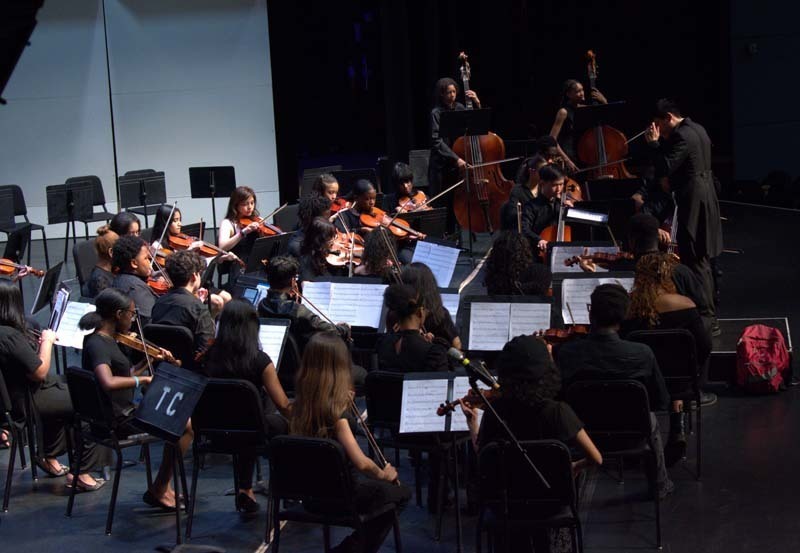 Student orchestra performing with conductor on stage.