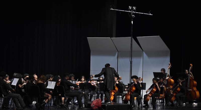 Student orchestra performing with conductor on stage.