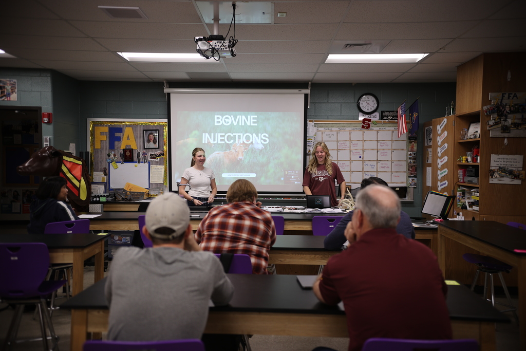 Students lead a classroom session on bovine injections, presenting to staff seated at lab tables during a student-led professional development activity.