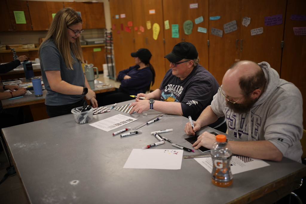 Student guides staff through a hands-on classroom activity, offering support as participants work on a lesson during a student-led professional development session.