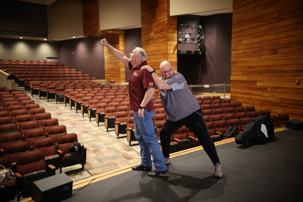 Staff members participate in a playful, hands-on activity on the auditorium stage, engaging in a student-led professional development session.