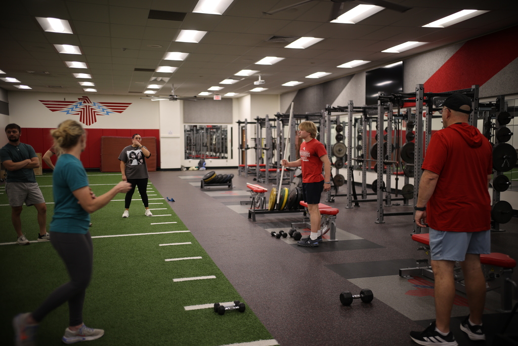 Student leads a strength training session in the high school weight room as staff participate and observe during a hands-on professional development activity.