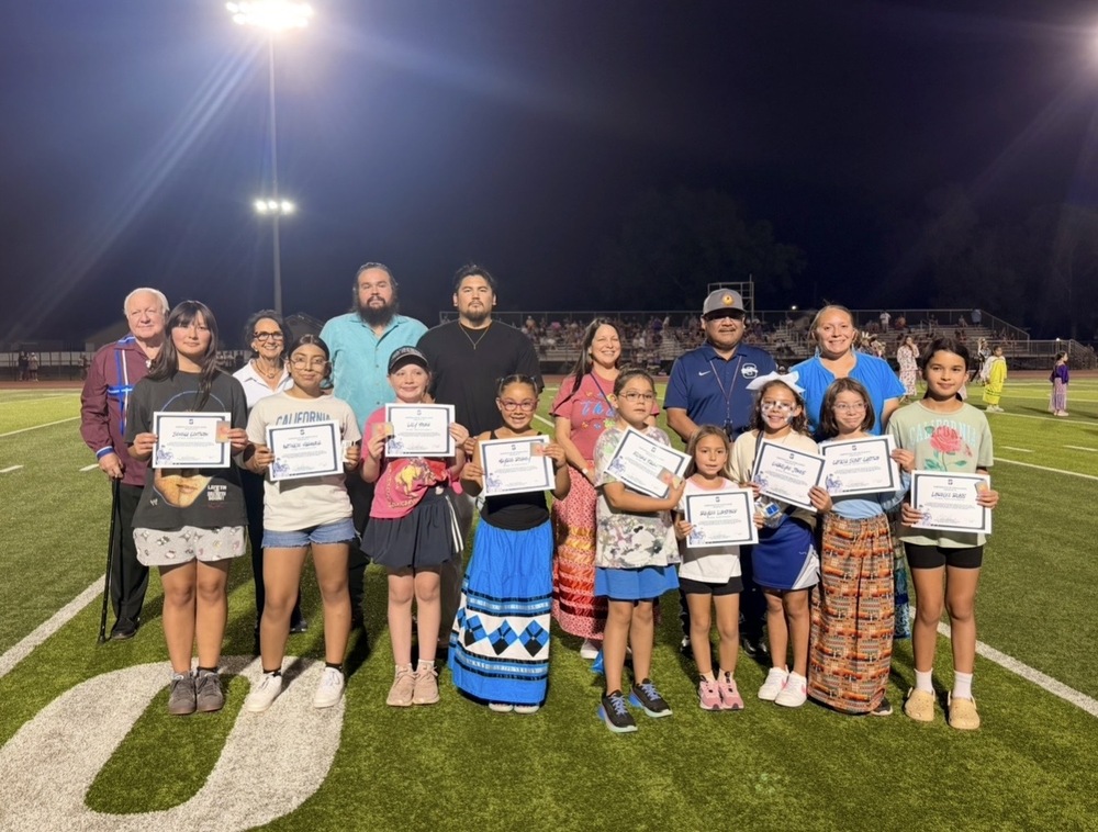 students on field with adults accepting certificates