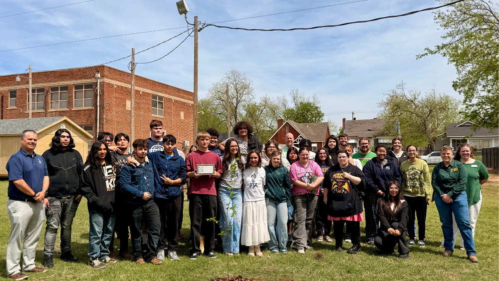 group of students standing outside with small tree