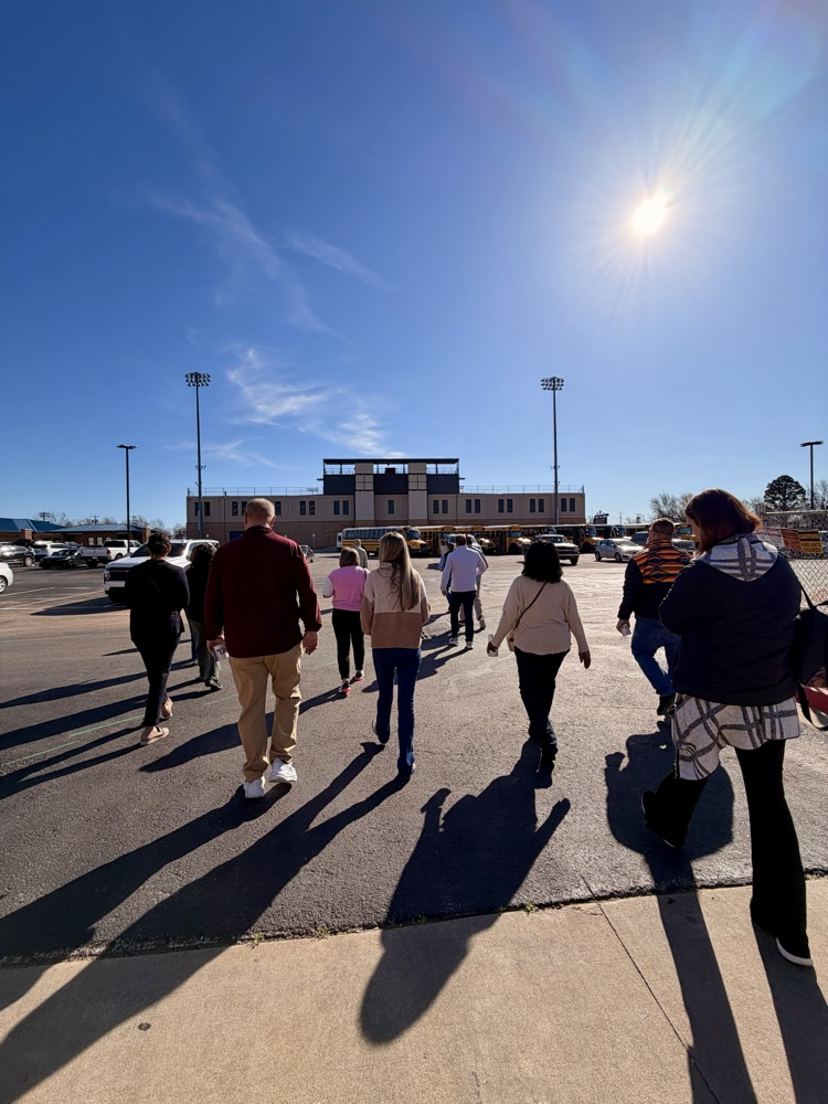adults walking across parking lot with stadium in distance 