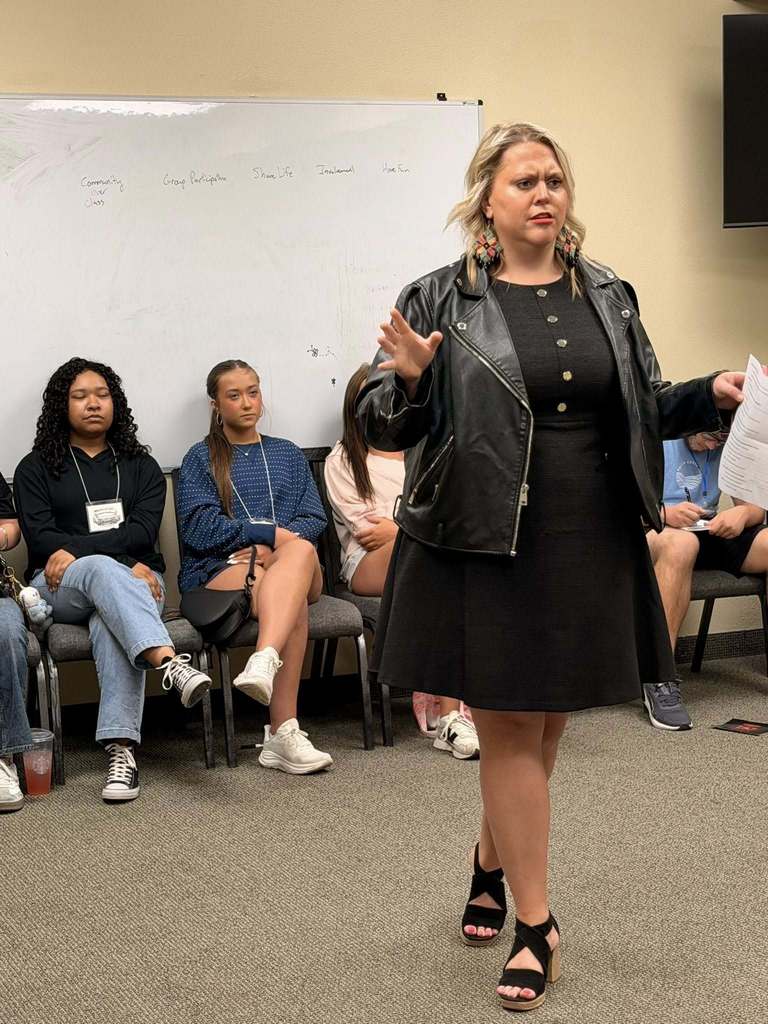 girl in black dress speaking to students