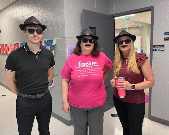 Two female teachers and one male teacher dressed in spy costume consisting of black hat, black sunglasses and fake moustaches.
