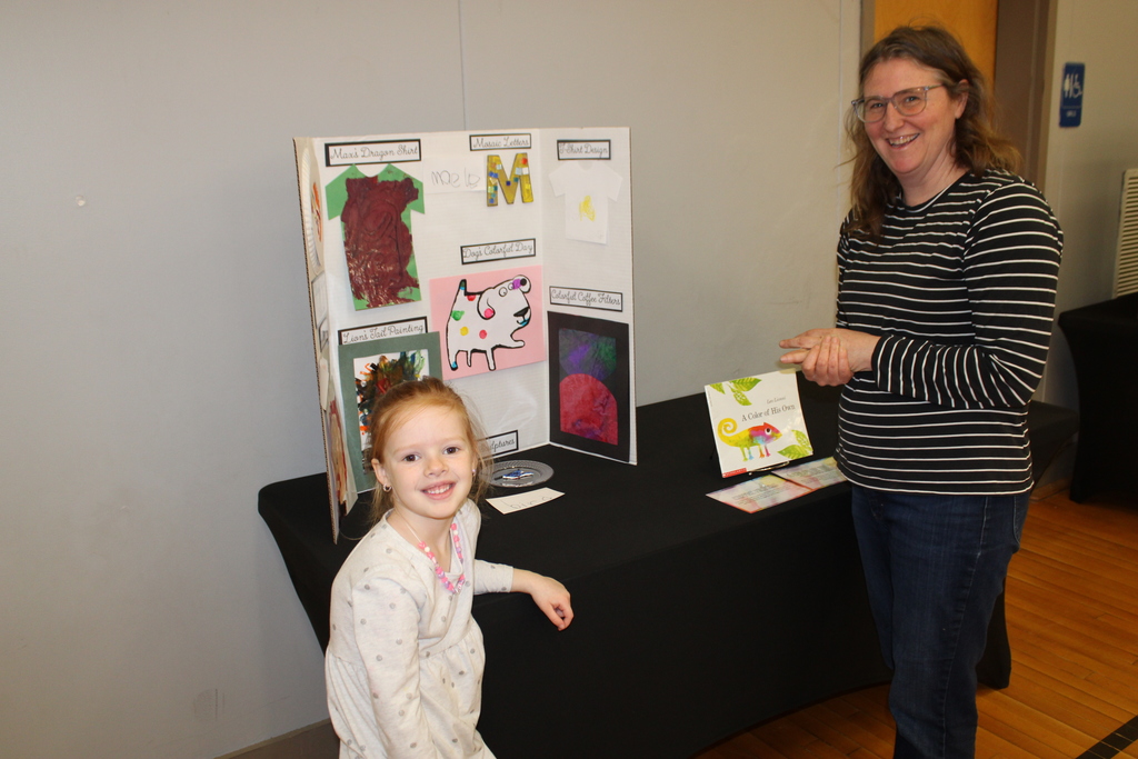 prek student and staff member stand in front of trifold art display