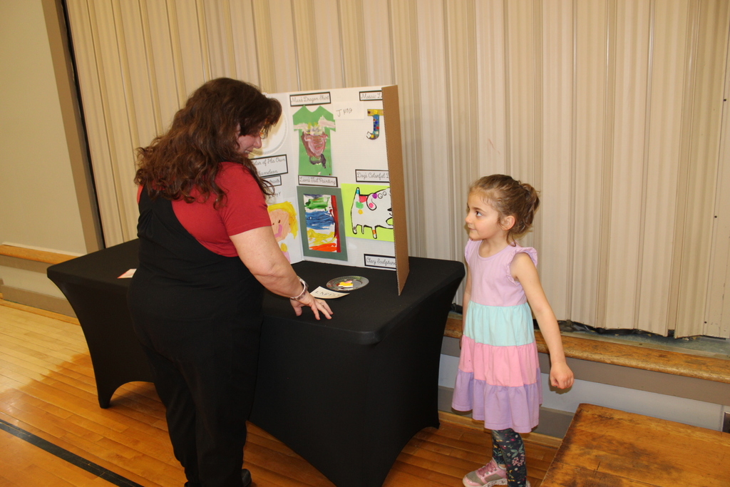 prek student explains art work while staff member listens