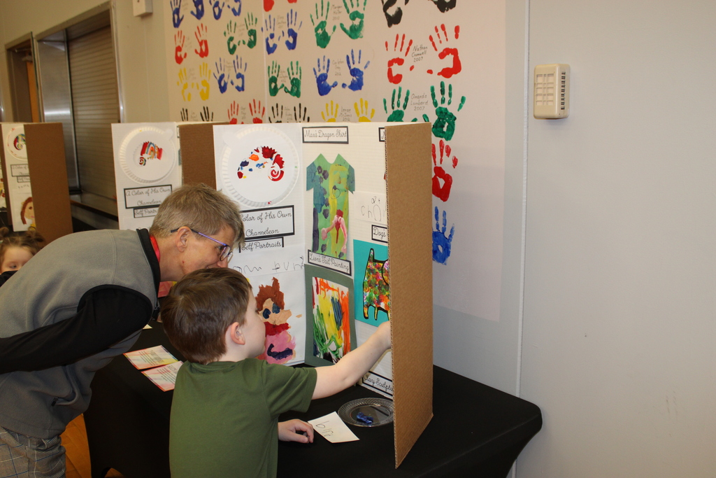 prek student points at art work and staff member looks on