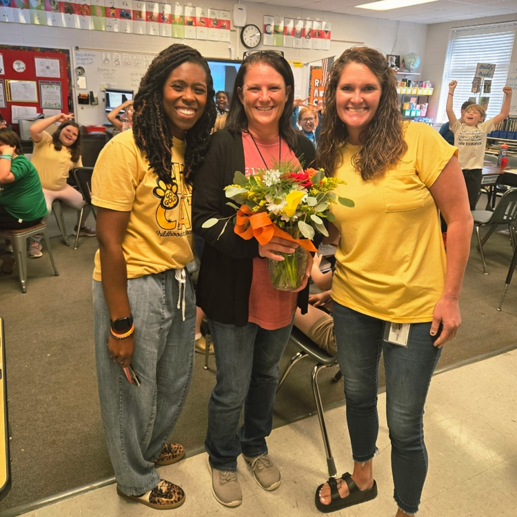 administrators pose with teacher of the year holding flowers in a classroom 