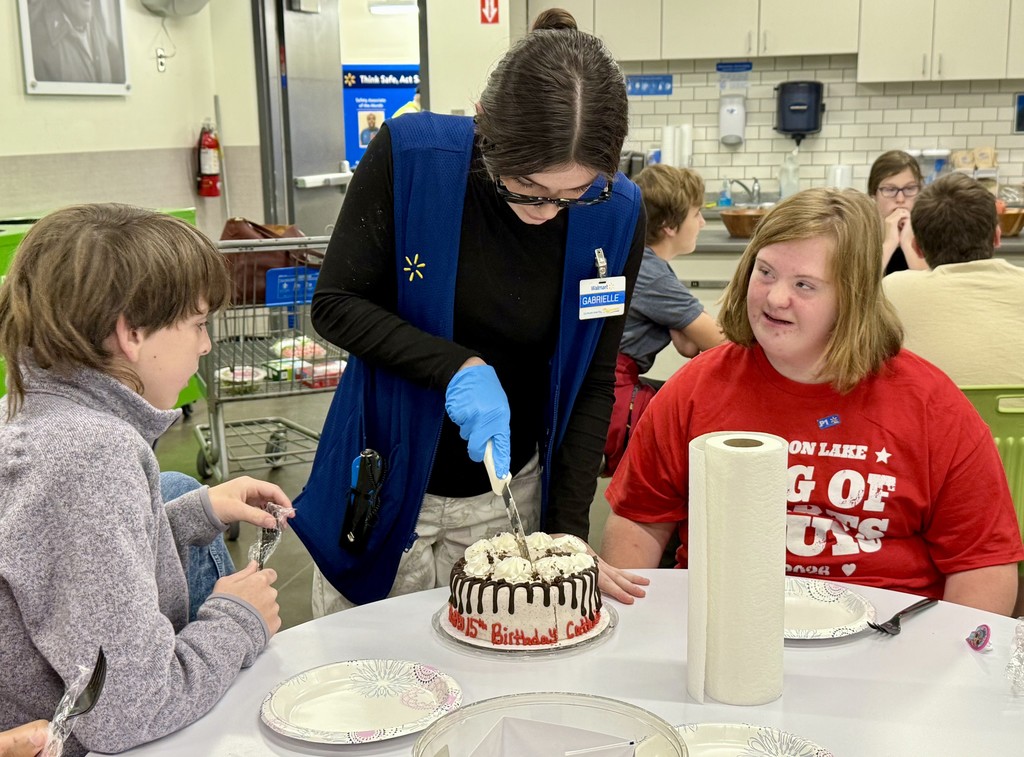A WalMart associate cuts the cake for two OMMS students at their visit to WalMart in Pelham.