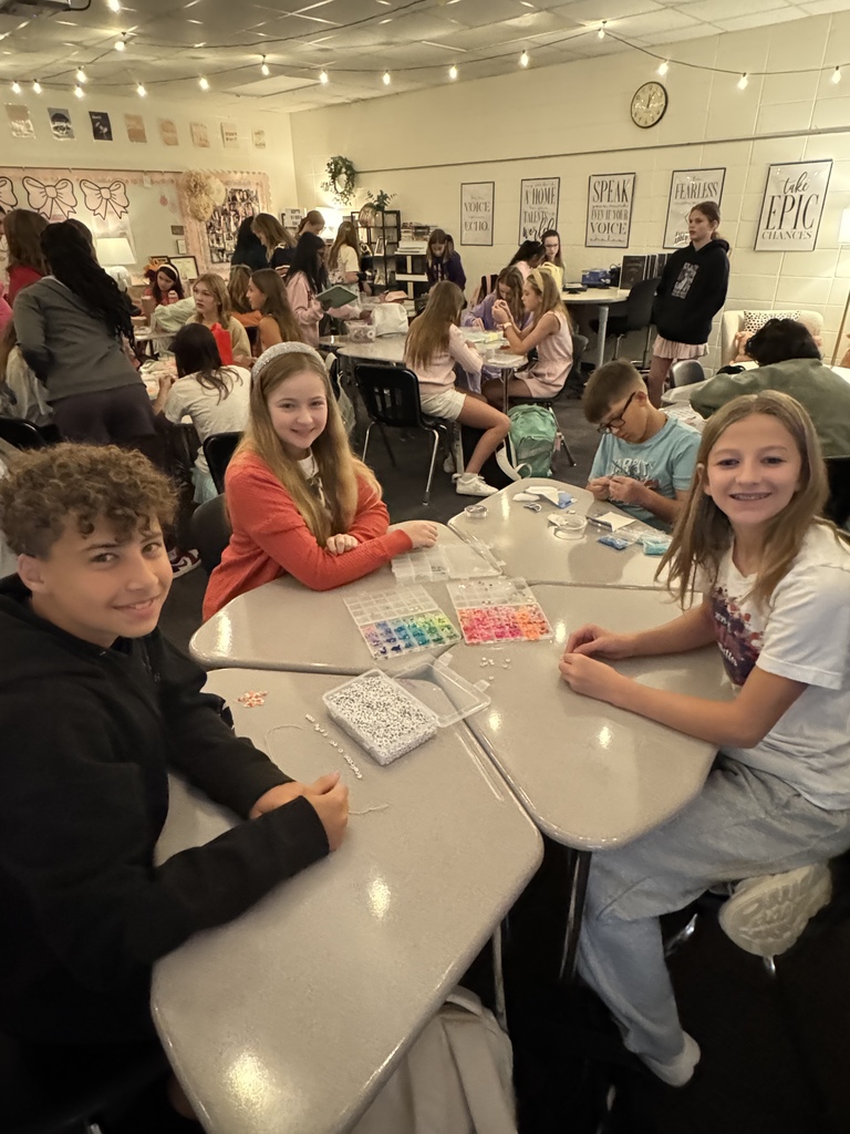 OMMS Swiftie Club students making bracelets together in small groups and smiling for the camera.
