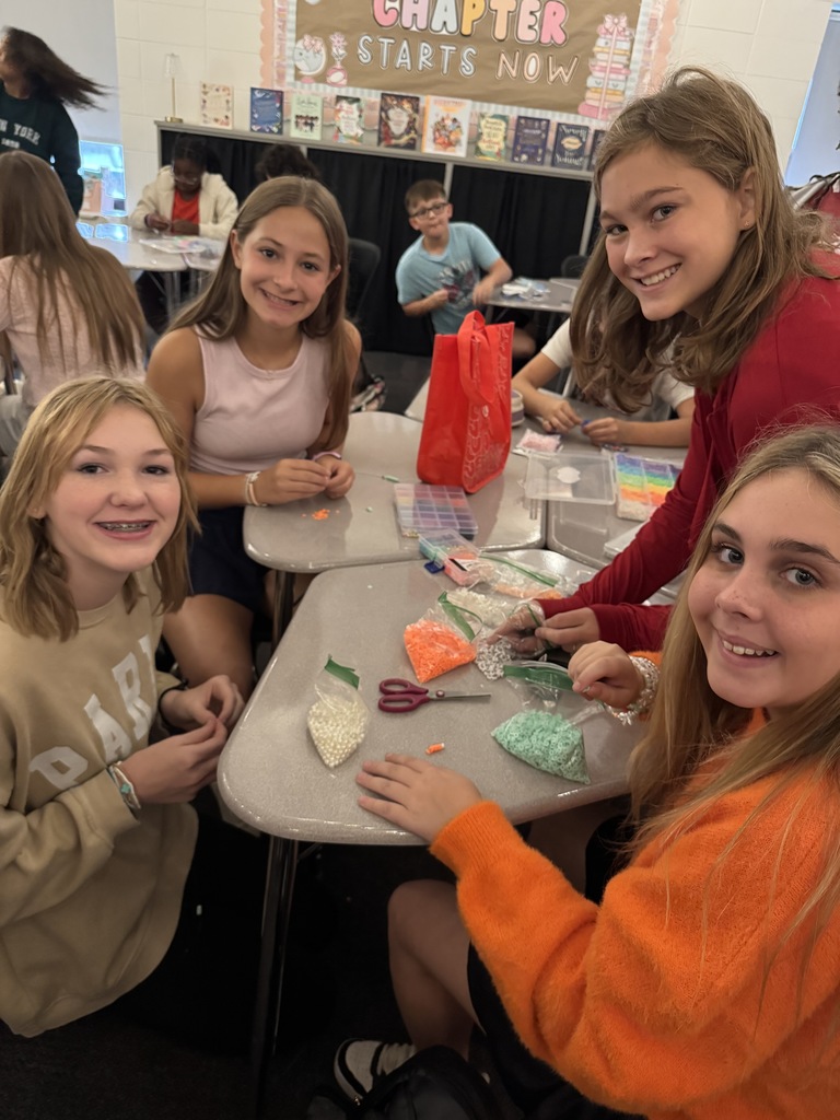 OMMS Swiftie Club students making bracelets together in small groups and smiling for the camera.