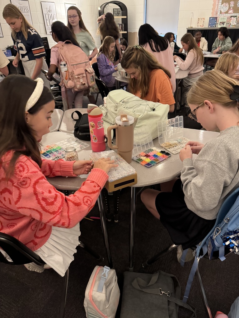 OMMS Swiftie Club students making bracelets together in small groups and smiling for the camera.