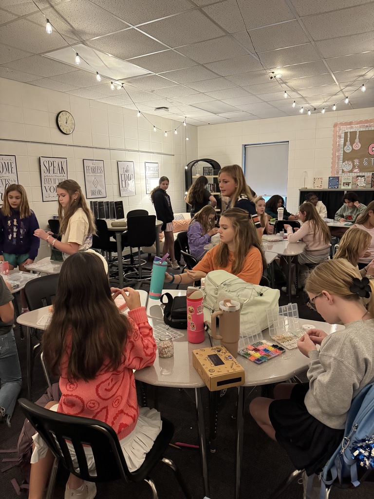 OMMS Swiftie Club students making bracelets together in small groups and smiling for the camera.