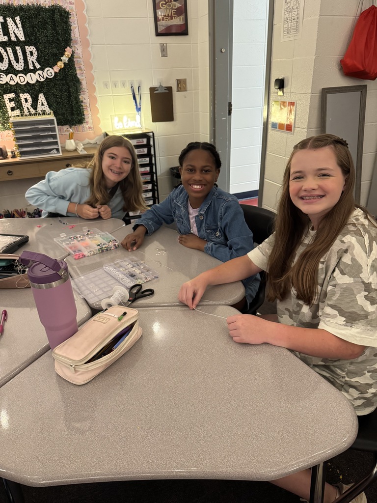 OMMS Swiftie Club students making bracelets together in small groups and smiling for the camera.