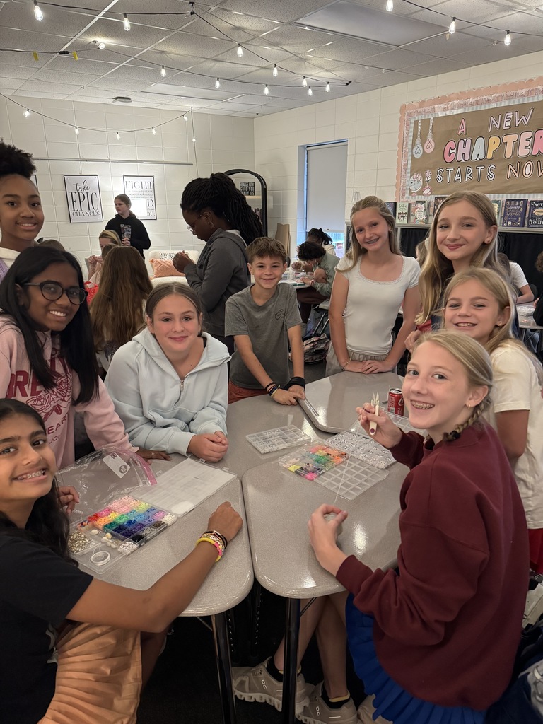 OMMS Swiftie Club students making bracelets together in small groups and smiling for the camera.