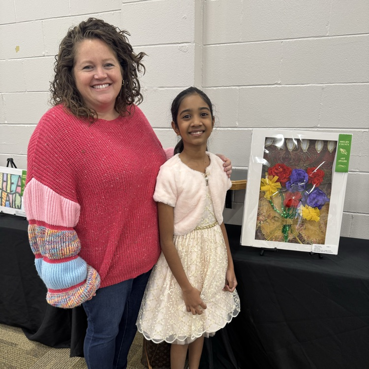 student and teacher pose beside student’s artwork 