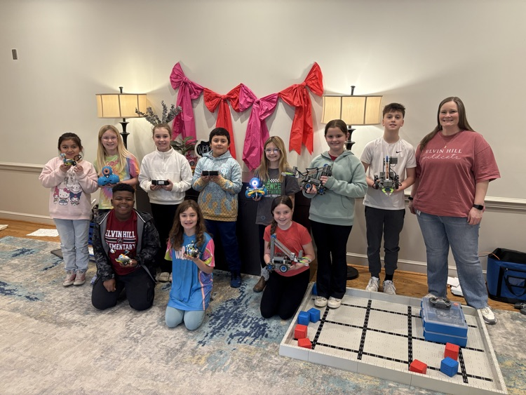 students pose with robots next to a vex field