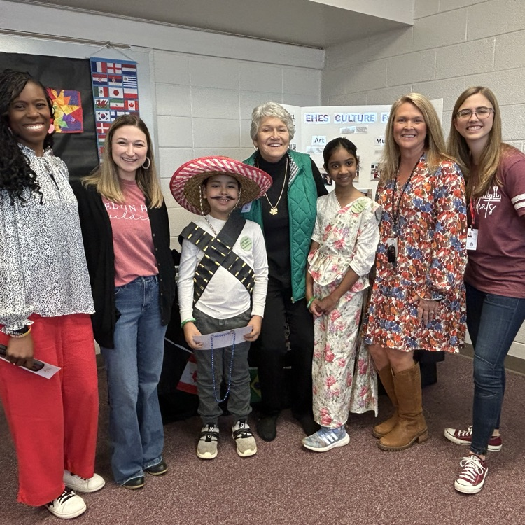 board members, administrator, teachers and students pose in front of cultural table