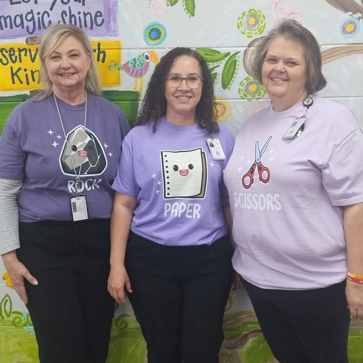 3 women in purple shirts that read paper rock scissors 