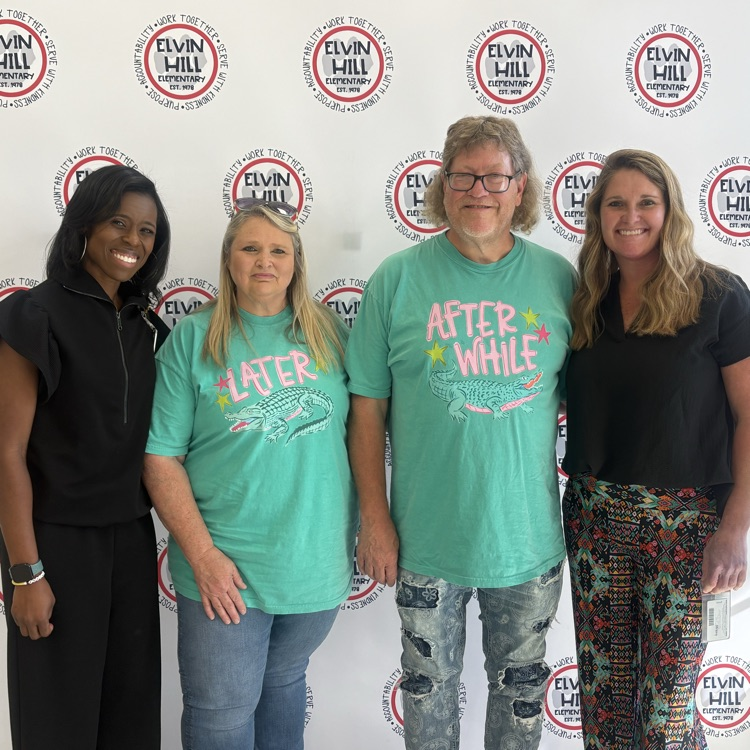man and woman posed with administrators in front of step and repeat backdrop with school logo