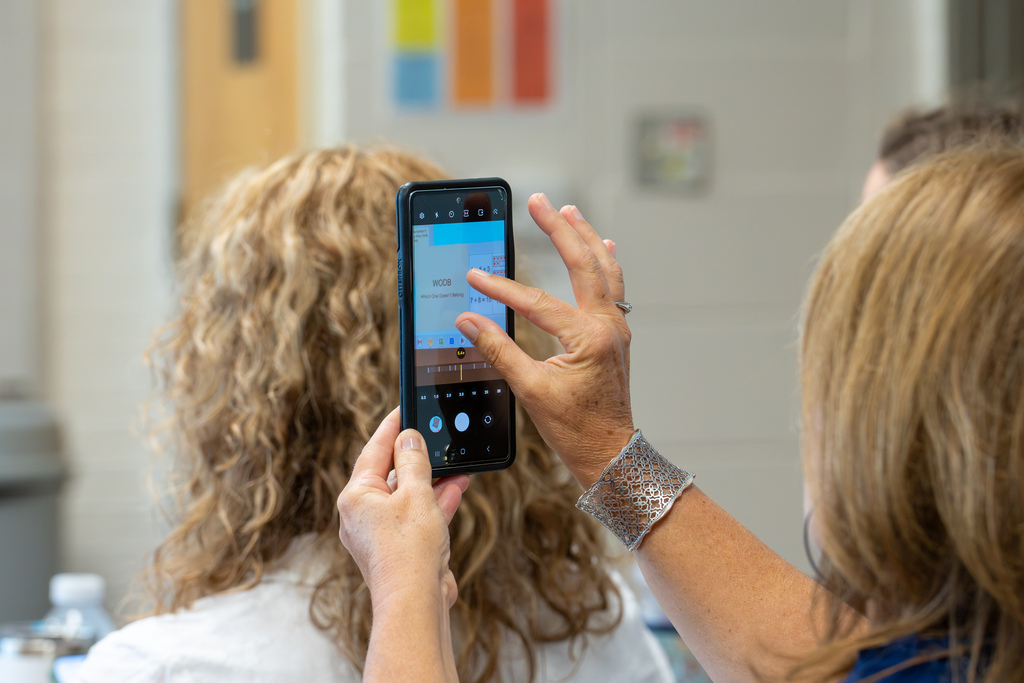 An educator uses a smartphone to photograph presentation materials during a professional learning workshop.