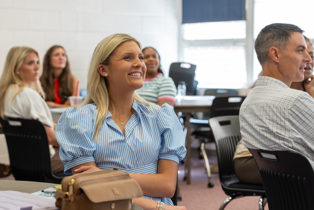 A teacher smiles while participating in a professional development session as colleagues listen during a classroom workshop.