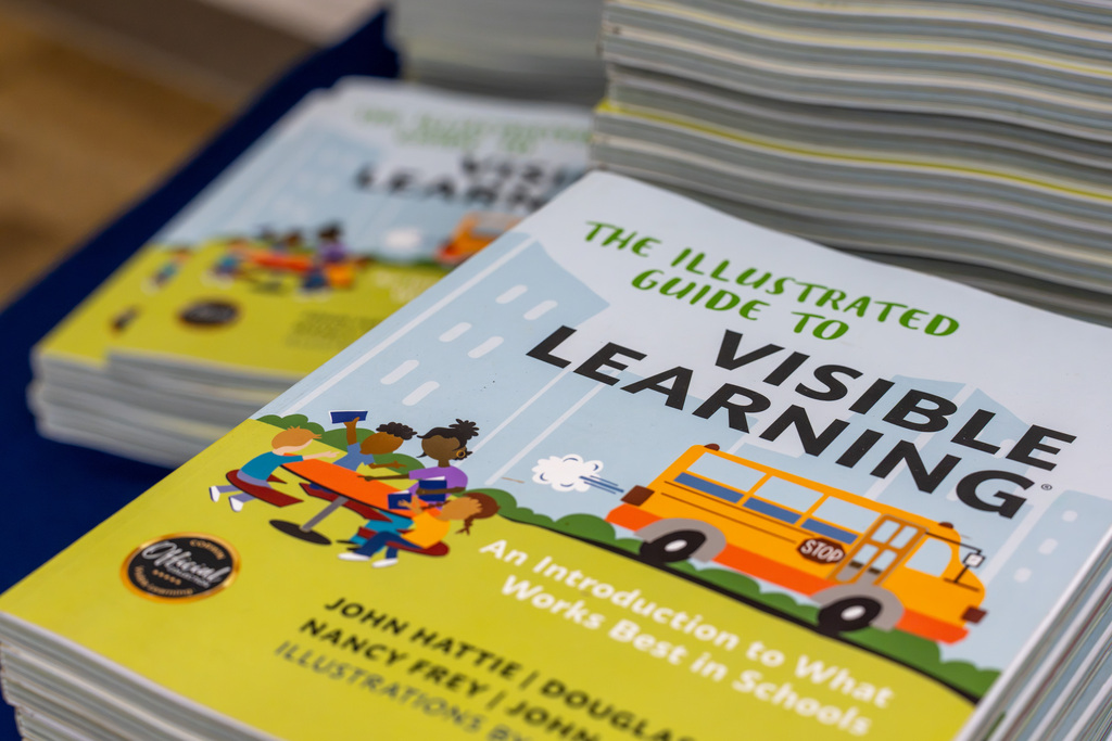 Copies of "The Illustrated Guide to Visible Learning" are displayed for participants at a professional development event.
