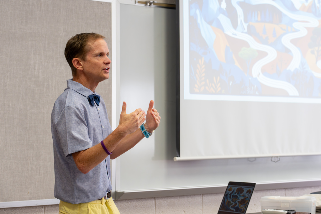 A presenter speaks to educators during a workshop while using a projected presentation to illustrate key concepts.