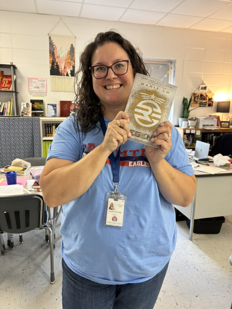 Mrs. Hutchings proudly holding up the book she is currently reading 