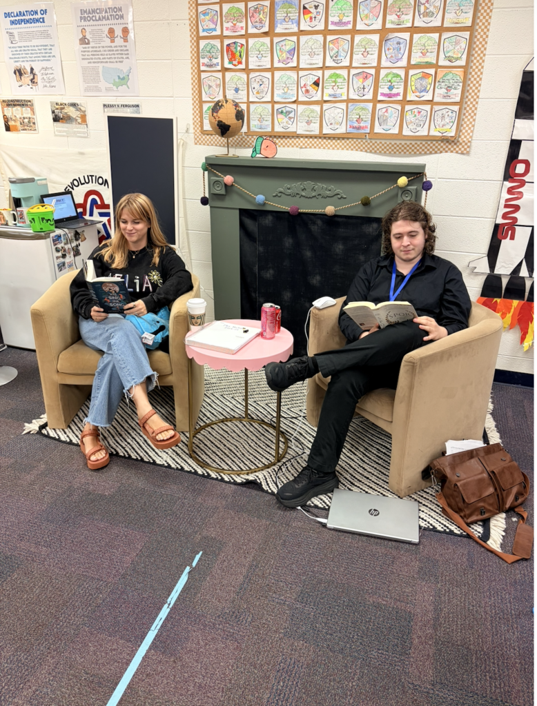 Mrs. Nichols and Mr. Hathorne sitting in chairs reading their current history books