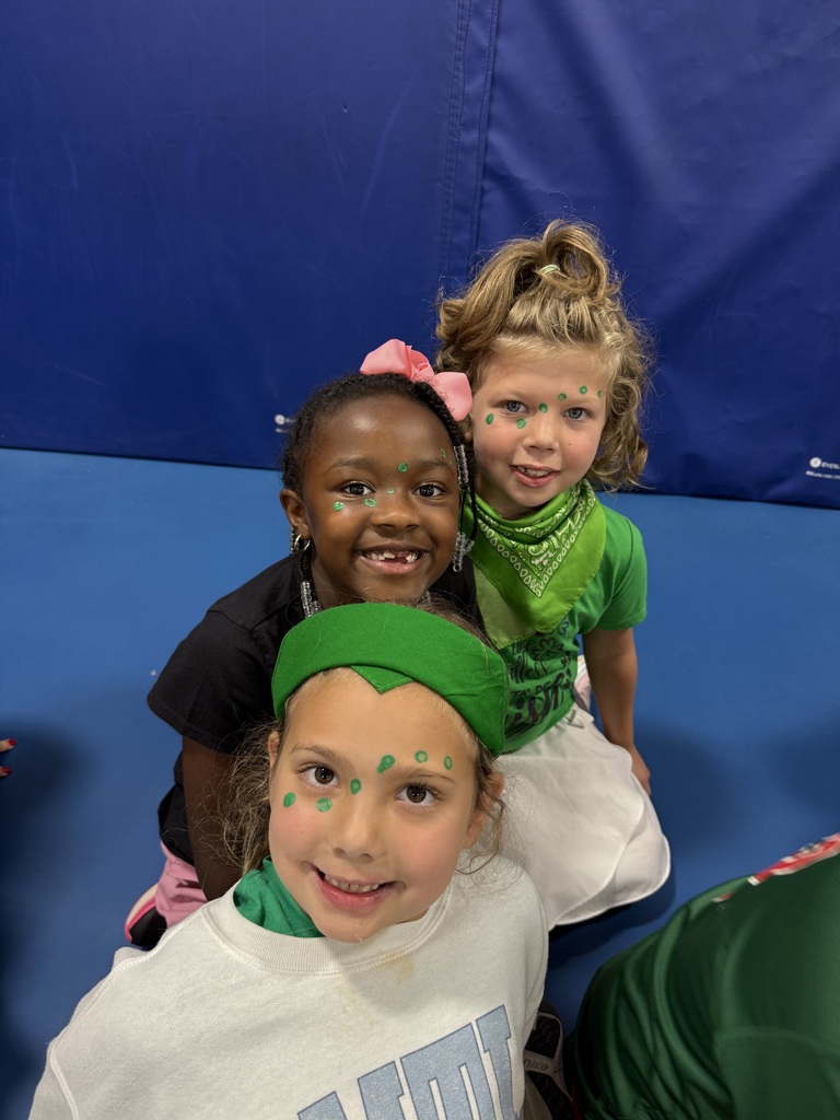 Three girls with green face paint smiling for a photo.