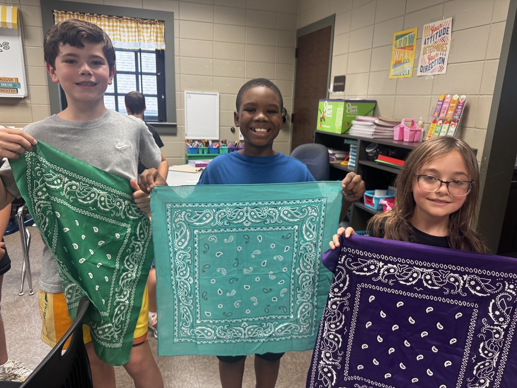 Three students smiling and holding up a colored bandana.