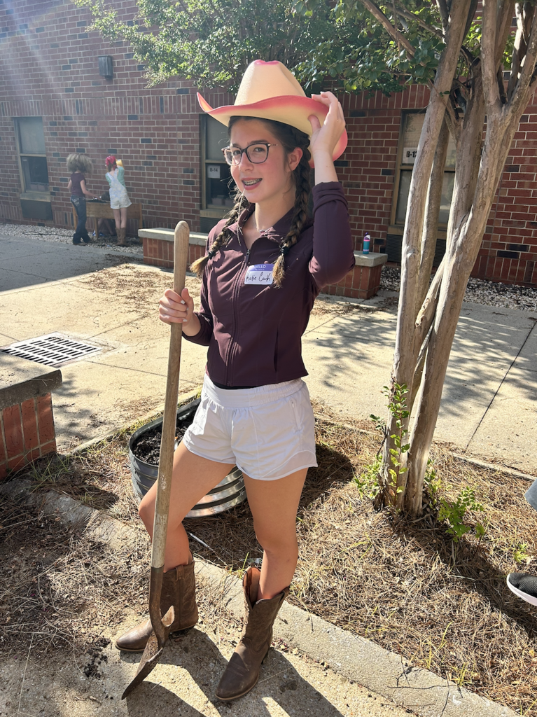 student wearing a cowboy hat poses for a photo in the courtyard with a shovel 