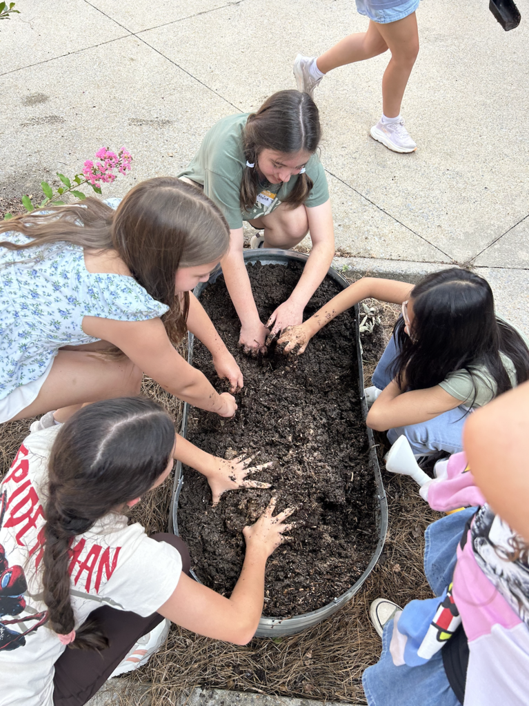 Students kneel around a metal tub planting seedlings