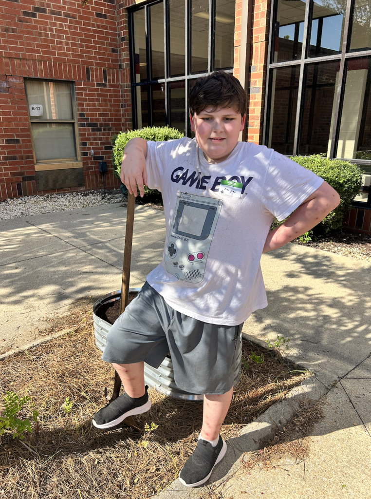 student in the courtyard is propped up on a shovel taking a break from his gardening work in the school courtyard 
