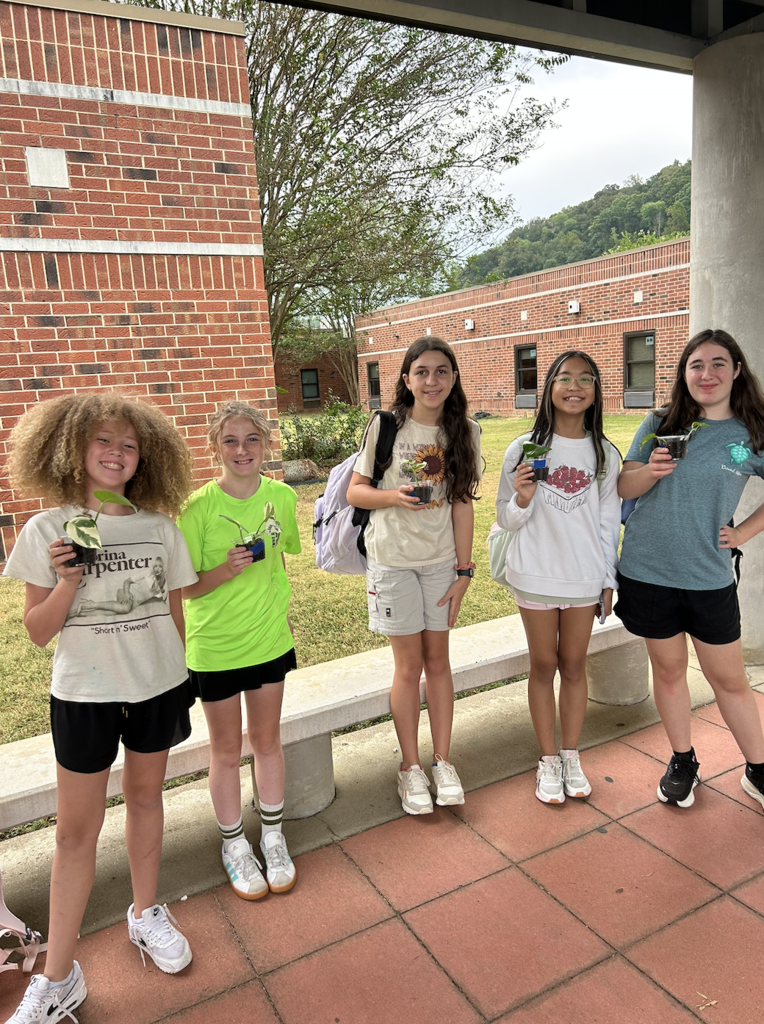 five students stand with their backpacks with young seedlings in their hands to take home and help grow