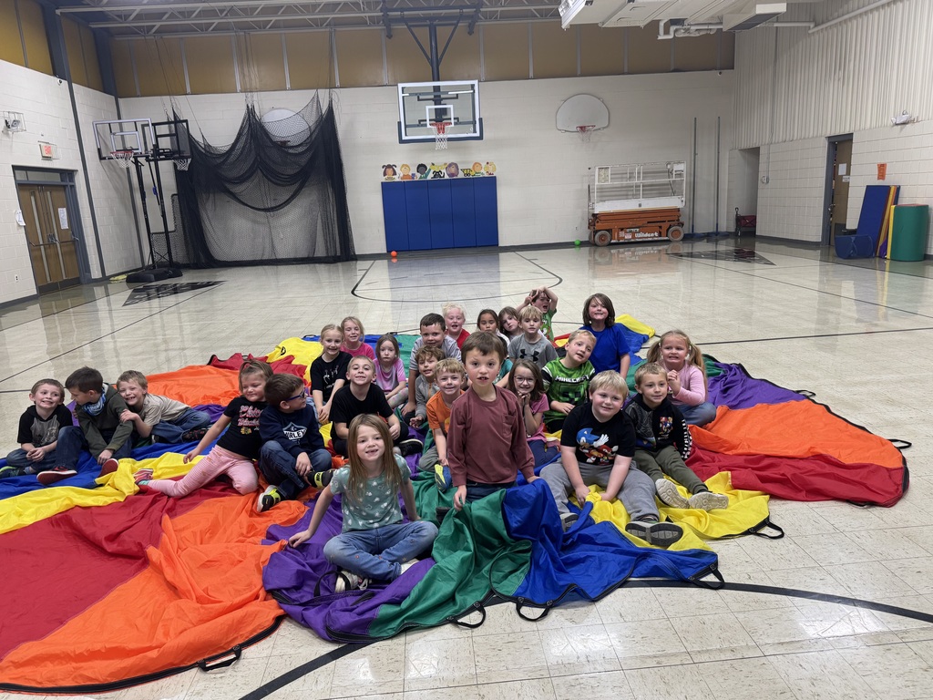 Elementary students sitting on rainbow parachute in PE