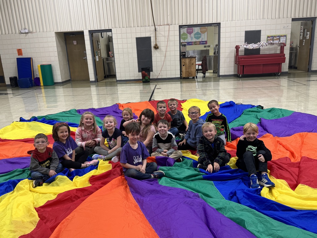 Elementary students sitting on rainbow parachute in PE