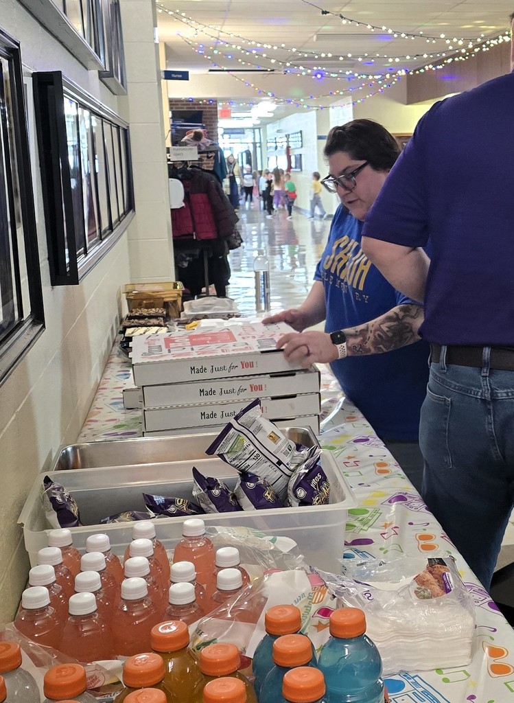 Junior high students sitting at tables in the main hallway as the staff serves them for their pizza party