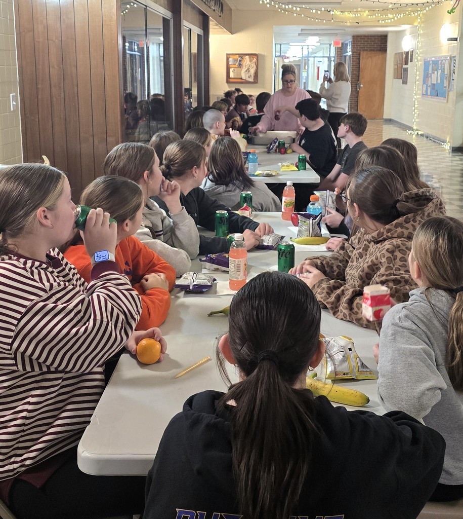 Junior high students sitting at tables in the main hallway as the staff serves them for their pizza party