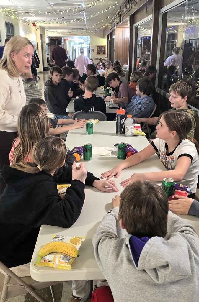Junior high students sitting at tables in the main hallway as the staff serves them for their pizza party
