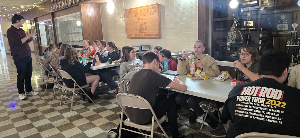 Junior high students sitting at tables in the main hallway as the staff serves them for their pizza party