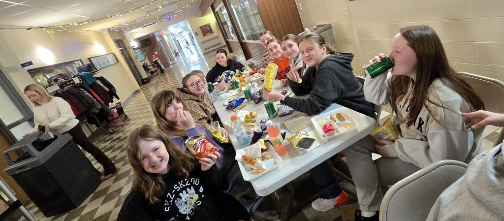 Junior high students sitting at tables in the main hallway as the staff serves them for their pizza party
