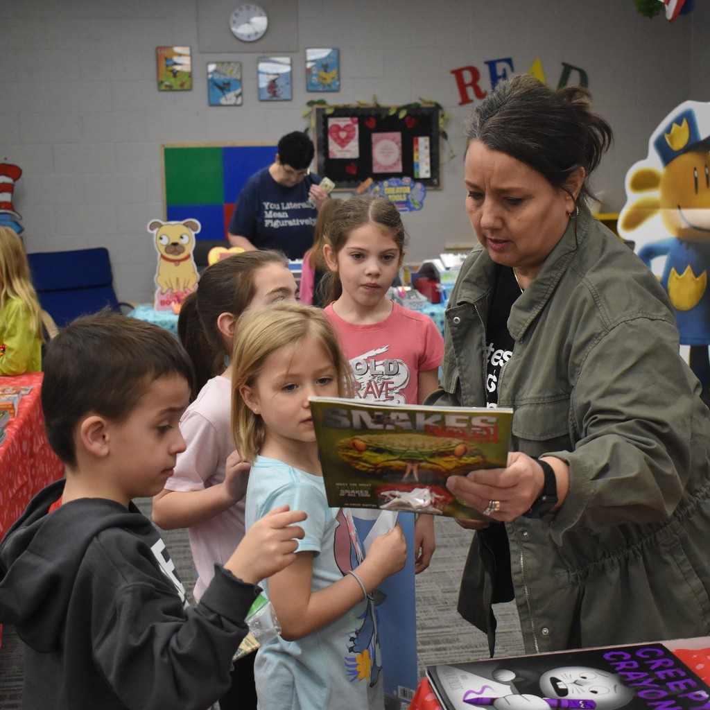 Mrs. Krabel looking at a book with students at the book fair