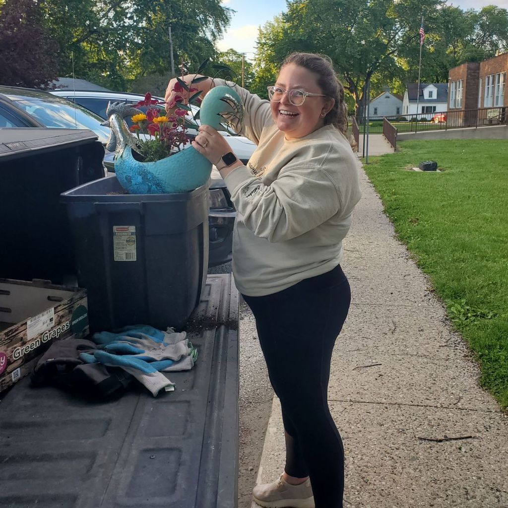 A woman with a big smile arranging her flowers in a blue rooster container