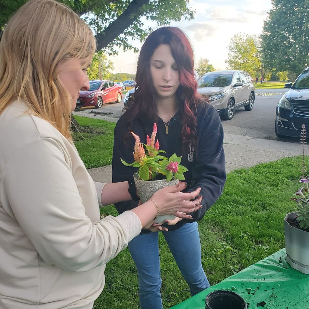 One woman with dirt on her hands handed a freshly-potted plant to another woman