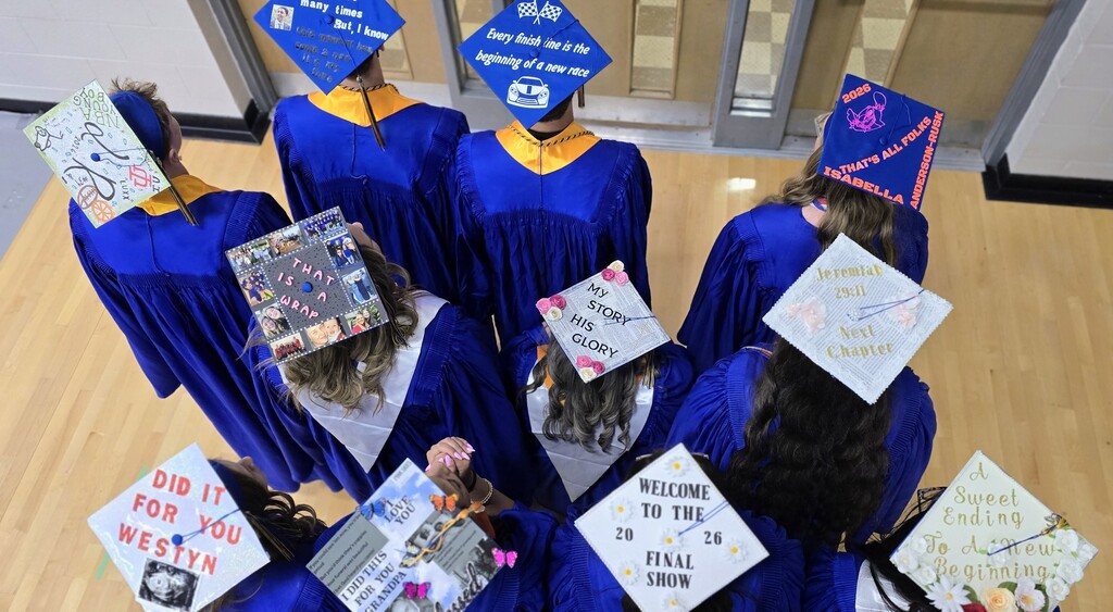 Photo showing the top view of decorated mortarboards for 11 seniors in blue graduation gowns